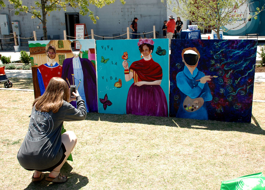 ColorPalooza attendees take photos in wooden cutout stands.  The wooden stands were located near a station to create kites.