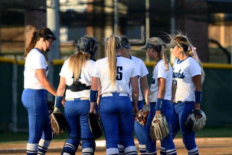 The varsity softball team huddle up at the beginning of an inning.