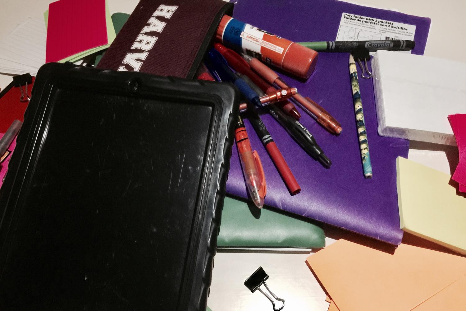 A collection of school supplies are laid out on a desk. Students are informed of what supplies are needed for each class on the first week of school.