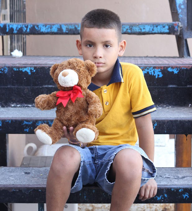 Nine-year-old Angel sits on the steps of the orphanage. He was playing with his toy bear. 