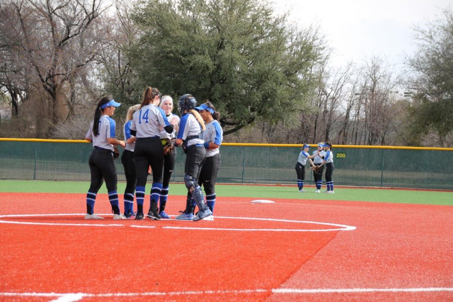 The softball team huddles around the pitchers mound. They were discussing a strategy prior to the start of the inning.