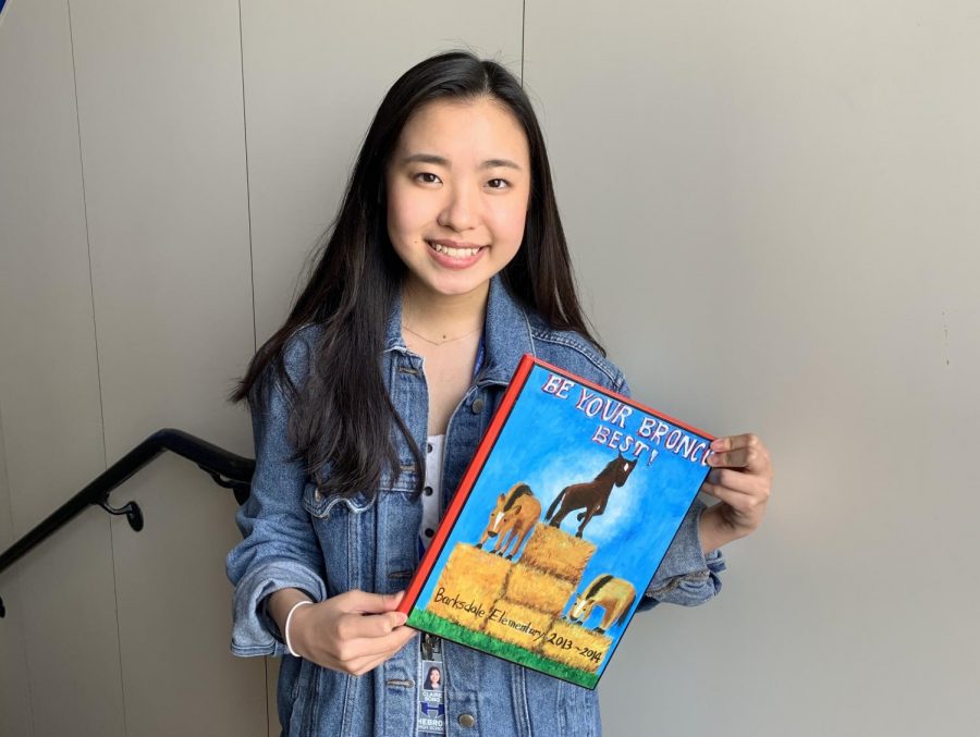  Junior Claire Song poses for a photo with the yearbook cover she painted in fifth grade. Song’s interest in art began in elementary school and carried on into high school. 