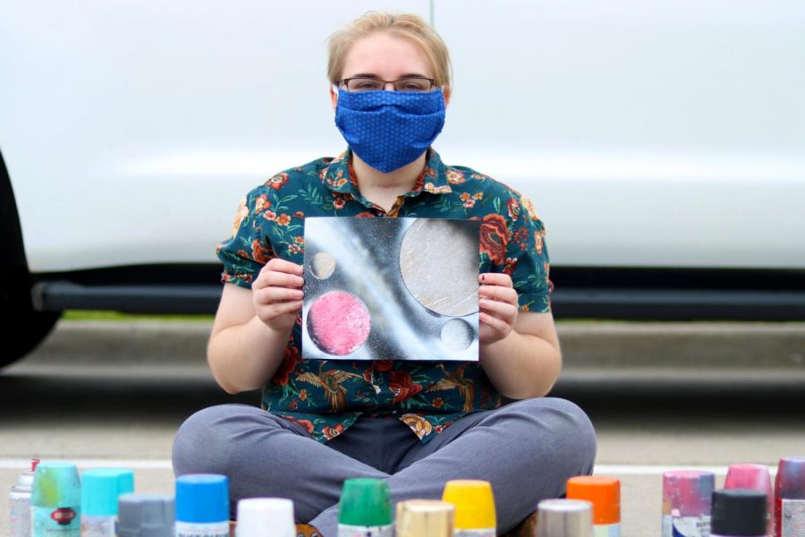 Senior Makena Butler poses with one of her spray paint pieces. She is wearing a mask to protect against Covid-19.