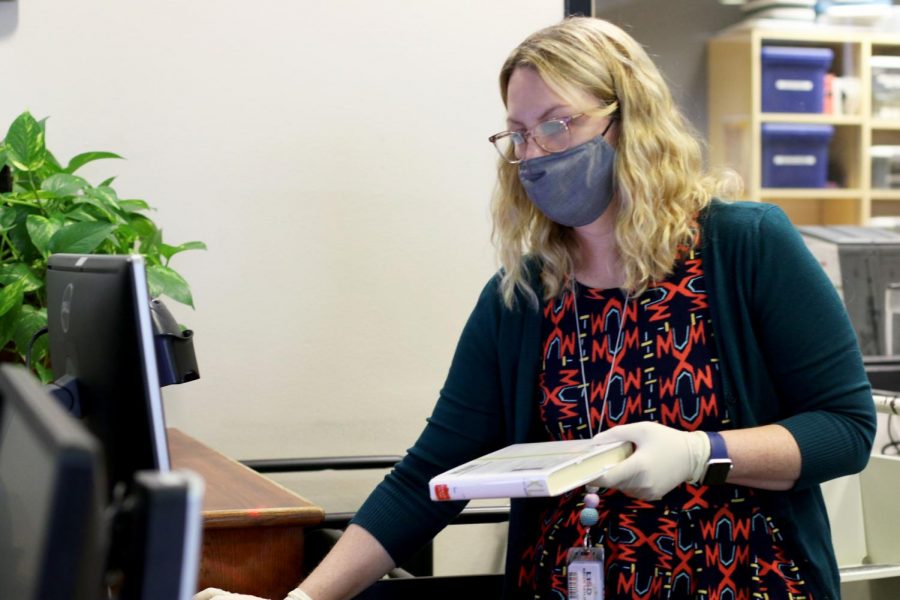 Librarian Kristi Taylor puts on gloves while wearing a mask, before checking books into the library system. Taylor said she wishes more students would say hello and strike up a conversation with her. “Speak when spoken to,” Taylor said. “Not everyone knows how to talk to someone who’s friendly. Say hi. I’m friendly and I talk a lot.”