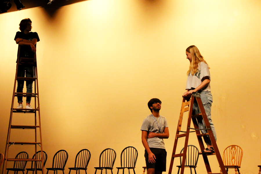 Junior Kyler Beck stands on a ladder and observes while senior Kaamil Thobani and junior Emma Foughty rehearse a scene in Act 1 of “Our Town.” The play is unique in the sense that it does not use a traditional set or props — in this scene, the actors on ladders are implied to be ‘upstairs’ in their respective homes. 