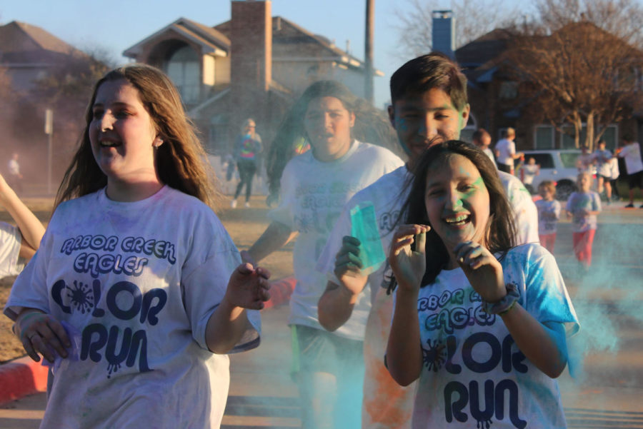 Students are sprayed with colored powder as they run. Several stations with colored powder were placed around the parking lot so people could spray runners as they passed.