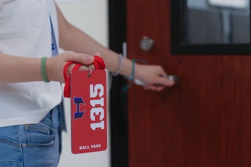 A student holds a hall pass while waiting outside a classroom.