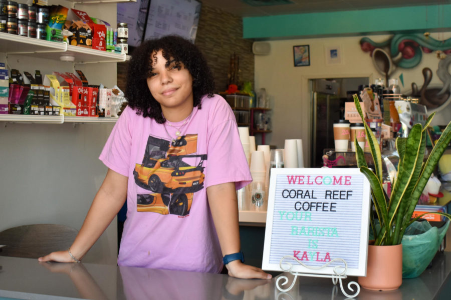 Kayla Bragg, a barista and merchandise designer for Coral Reef Coffee Company, grins at the front counter of the shop. [The environment] is really relaxed, Bragg said. People often come in here to work or study. Her favorite drink on the menu is the coconut mint matcha.