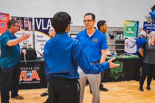 

A representative from the Virtual Learning Academy speaks with an attendant of the 2022 LISD in person job fair in the gym. The event showcases all schools in LISD, as well as multiple departments in the district, to potential applicants.