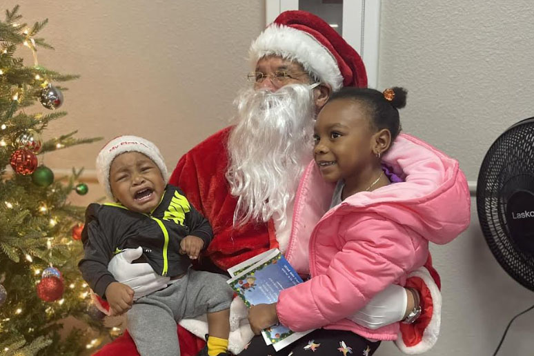 A volunteer dressed as Santa holds two children. At Christmas Cheer, volunteers can also pass out hot chocolate, coffee and cookies. 