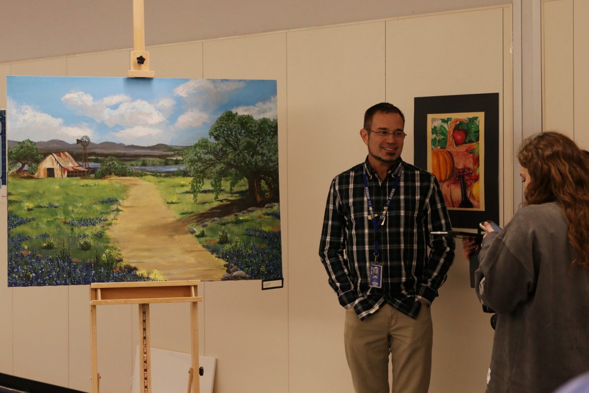 Spanish teacher Larry Horton shows off his painting to some students. This painting was displayed along with another of his landscape art pieces.