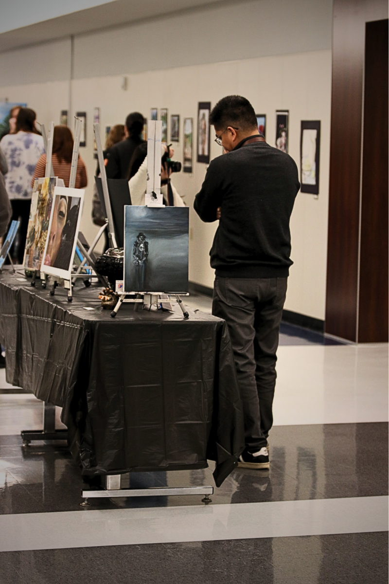 Orchestra teacher Matthew Cautivar looks at some of his students’ work. A few of his students were at the gallery; some submitted artwork and some played music.