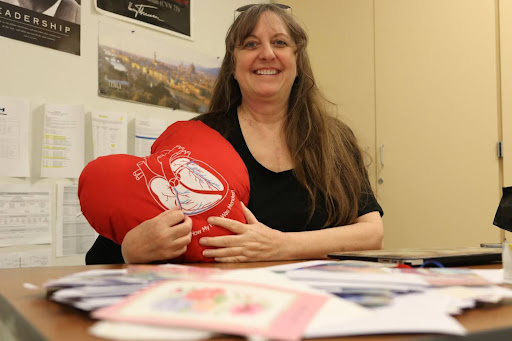 Special education teacher Deborah Corbet poses with a heart pillow she received in the hospital, with letters she received laid out on her desk. Corbet has a long scar across her chest from her heart surgery.