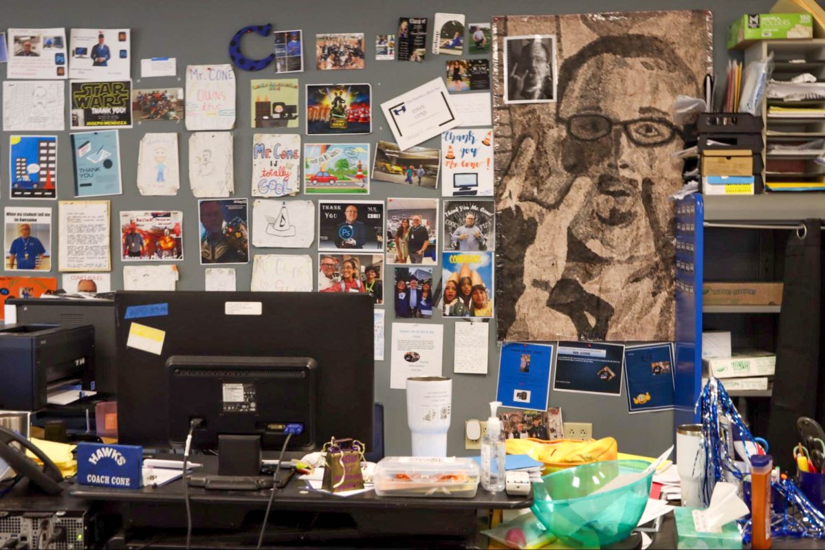 Business teacher David Cone hangs up projects from students, including a watercolor painting from an art class 24 years ago. He said he likes to keep photos of past students and co-workers who have passed away on his wall. “It reminds me [to] make sure I’m treating people right,” Cone said. “You never know if it’s gonna be [the] last time you see them.”